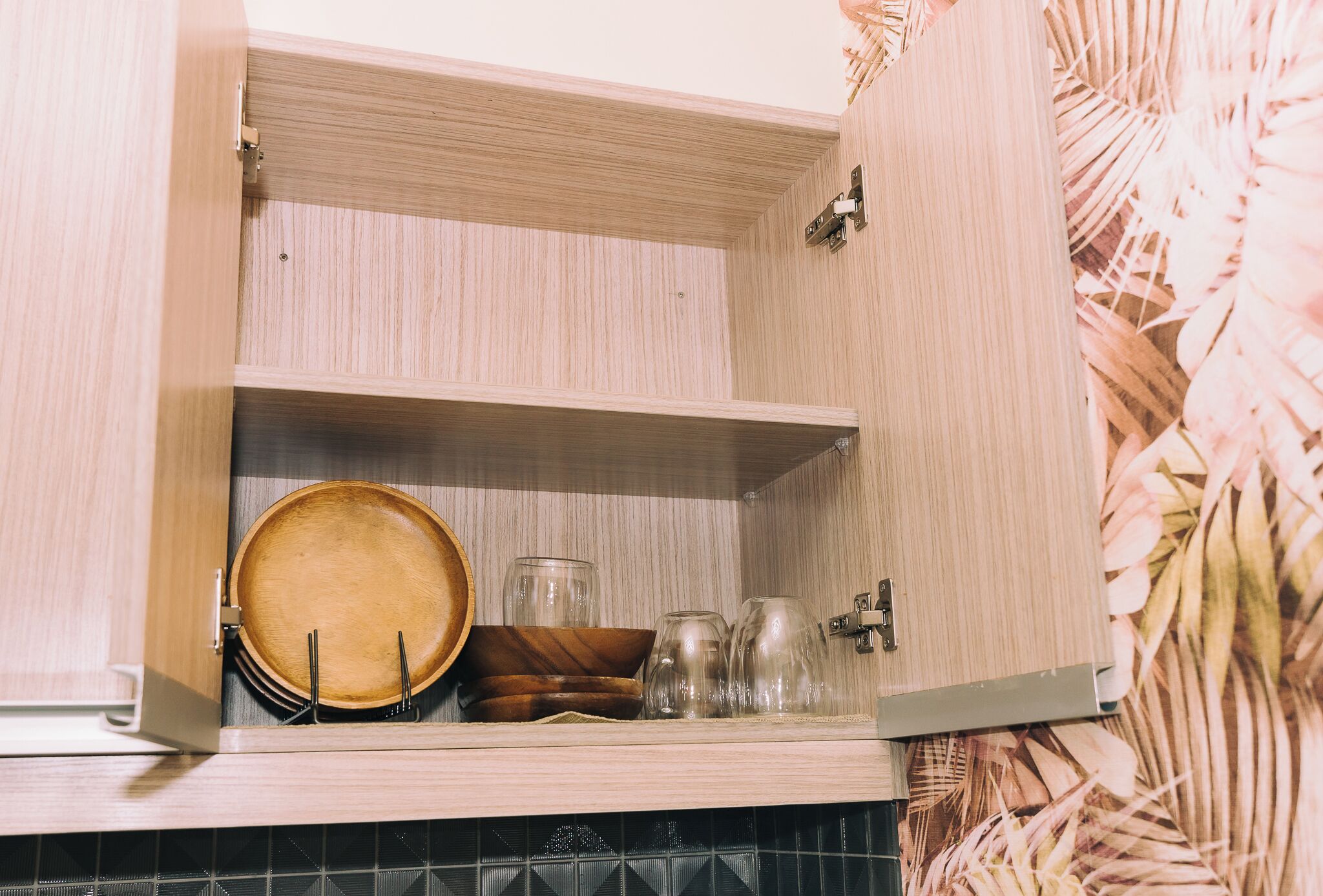 Un armario de cocina con estantes de madera, que contiene un plato de madera, cuencos y frascos de vidrio.