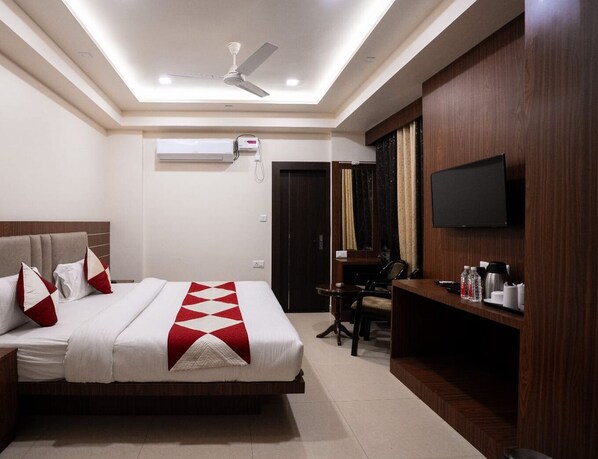 Habitación de hotel con cama, escritorio, silla, televisor y aire acondicionado.