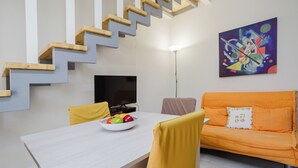 A modern living room with a staircase, a dining table with fruit, a sofa, and a painting on the wall. - Lo Stagnone Apartments (Marsala)