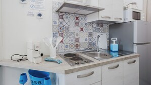 A kitchen with a microwave, stove, sink, and various kitchen utensils. There are also blue cups and a coffee maker on the counter. - Lo Stagnone Apartments (Marsala)