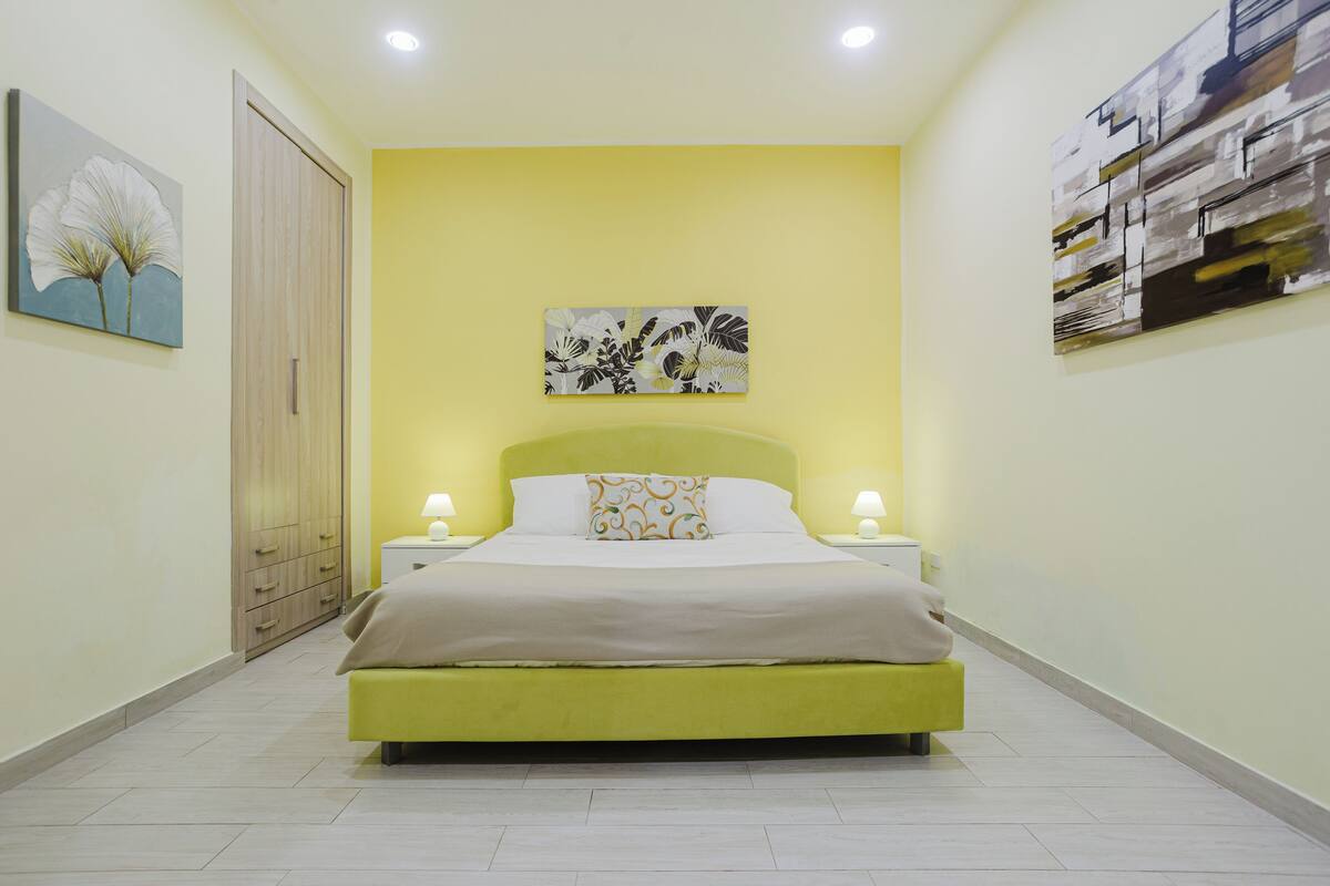 A bedroom with a bed, bedside tables, a wardrobe, and artwork on the walls.