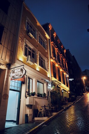 Een hotel met een bord waarop 'BDK HOTEL' staat, met een klassiek gevelontwerp, meerdere ramen en balkons, en een kinderkopjesstraat ervoor.
