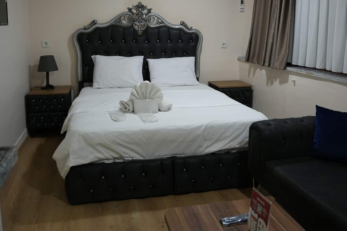 A bedroom with a large bed, a bedside table, a nightstand, a wooden coffee table, and a window with curtains.