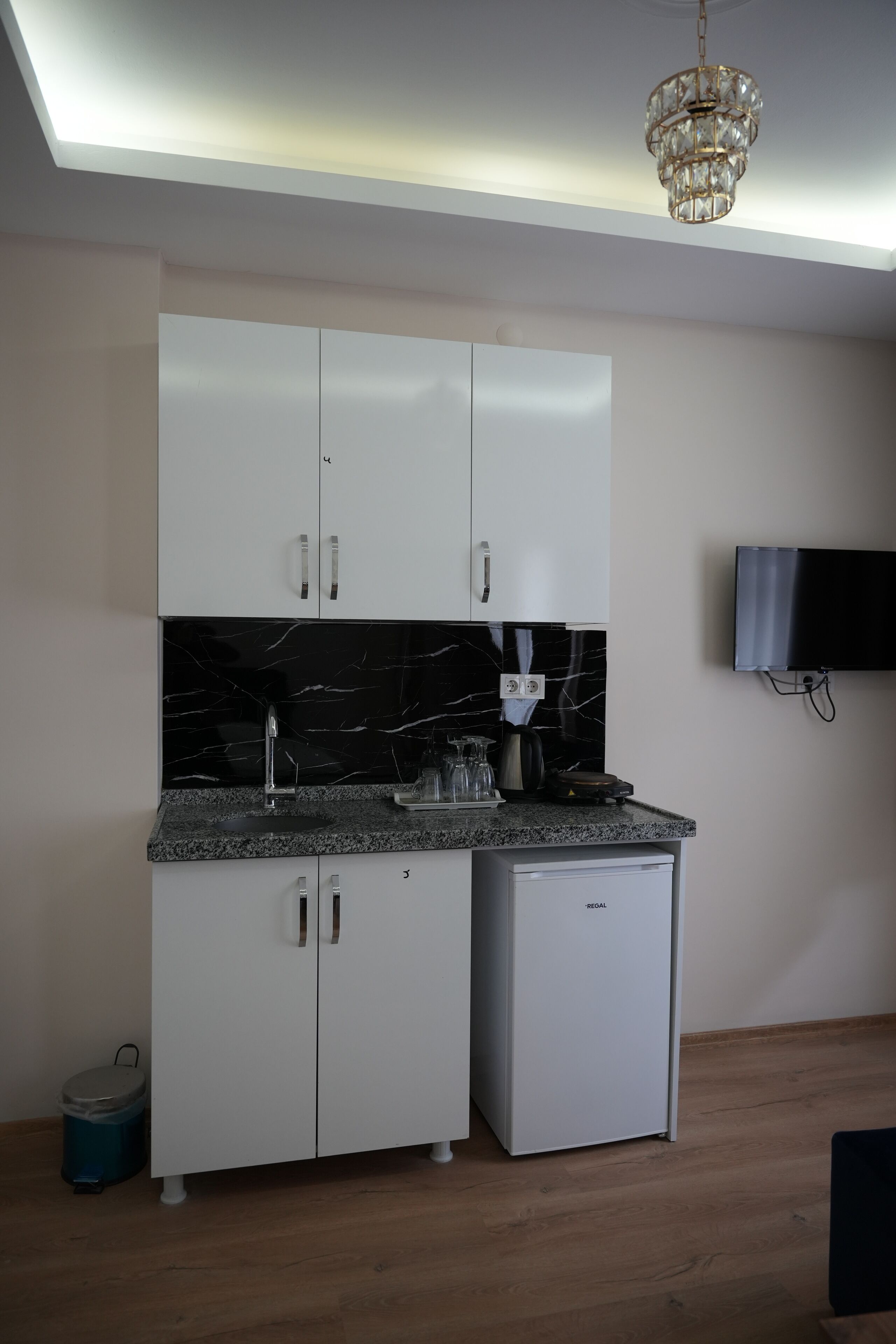 A compact kitchen with white cabinets, a black marble backsplash, a built-in refrigerator, and a ceiling light fixture.