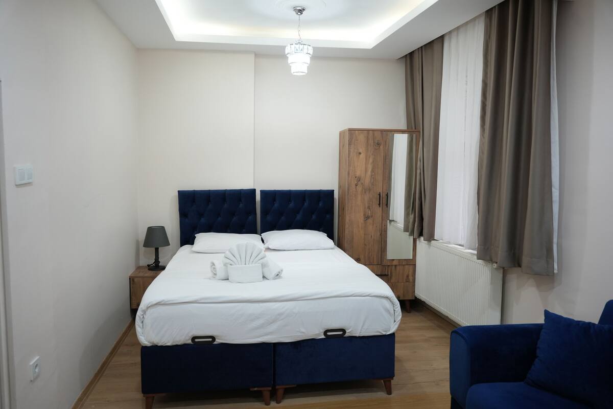 A bedroom with a large bed, a wooden wardrobe, a blue armchair, and a skylight.