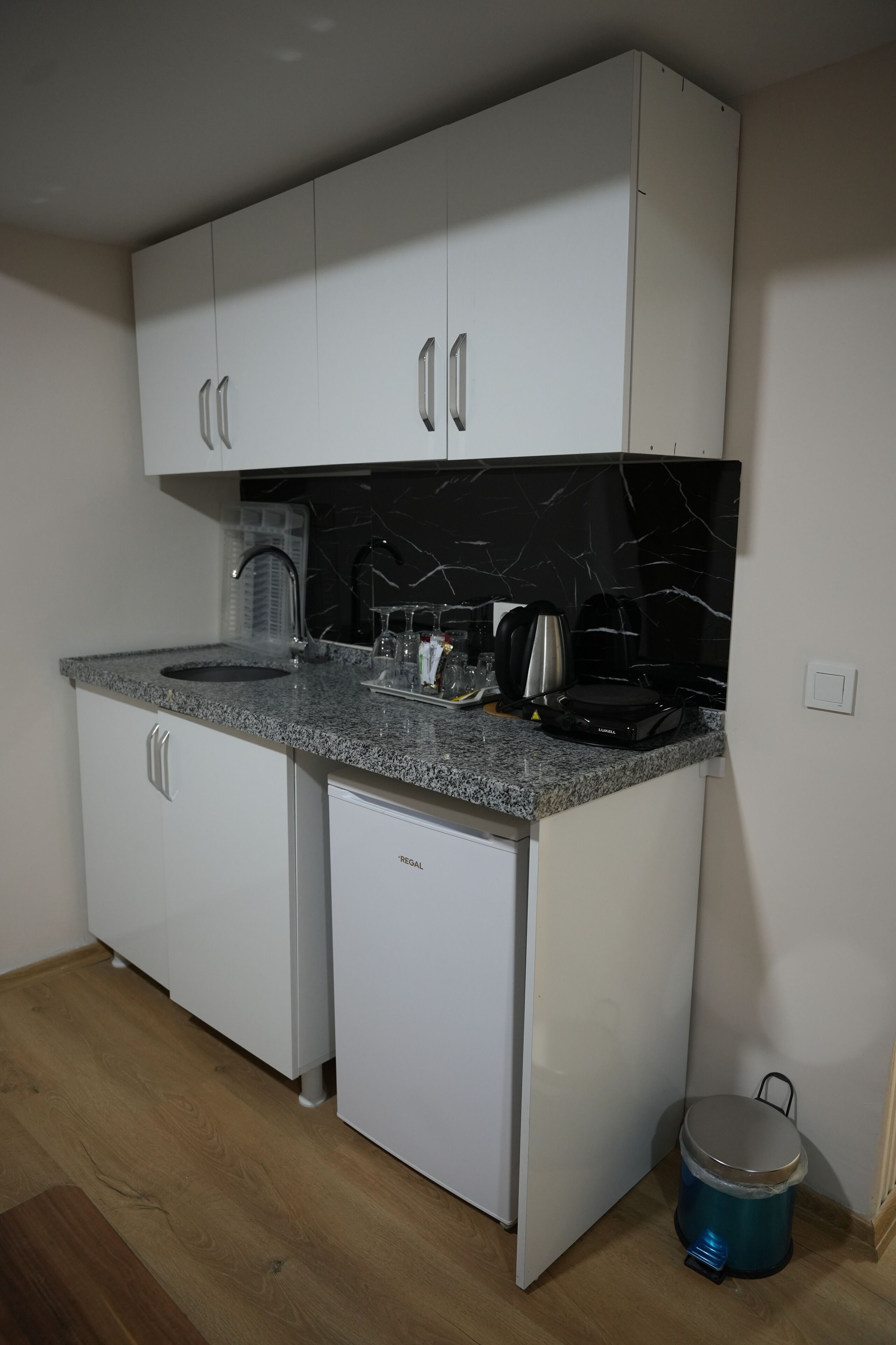 A compact kitchen with white cabinets, a granite countertop, and a black marble backsplash.