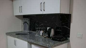 A compact kitchen with white cabinets, a granite countertop, and a black marble backsplash.
