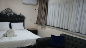Ett hotellrum med en säng, en soffa i mörk färg, ett soffbord i trä och ett fönster med gardiner.