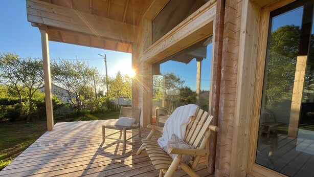 A wooden deck with two rocking chairs and a glass door leading to a covered area. - Chalet bois cœur Cévennes (Saint-Sauveur-Camprieu)