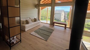 A spacious room with a wooden floor, a white sofa, a large window, and a wooden ceiling. - Chalet bois cœur Cévennes (Saint-Sauveur-Camprieu)