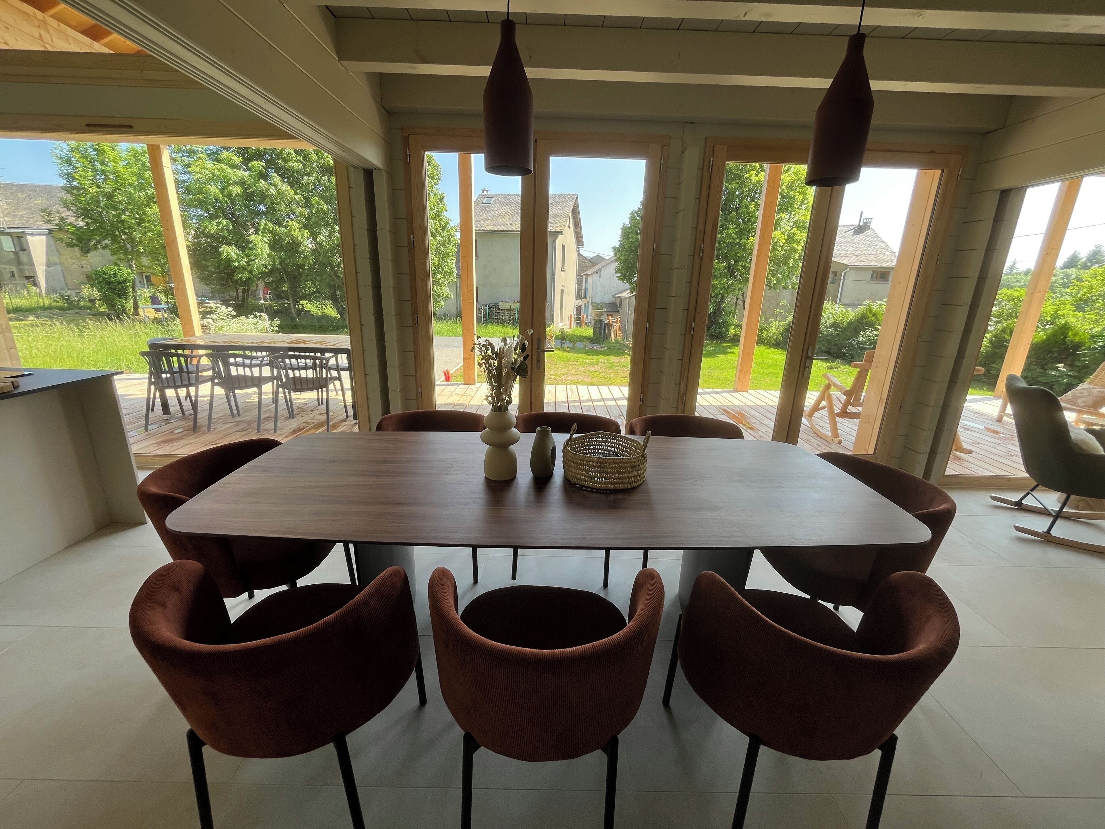 A dining area with a large wooden table, six brown chairs, and a vase with dried flowers.