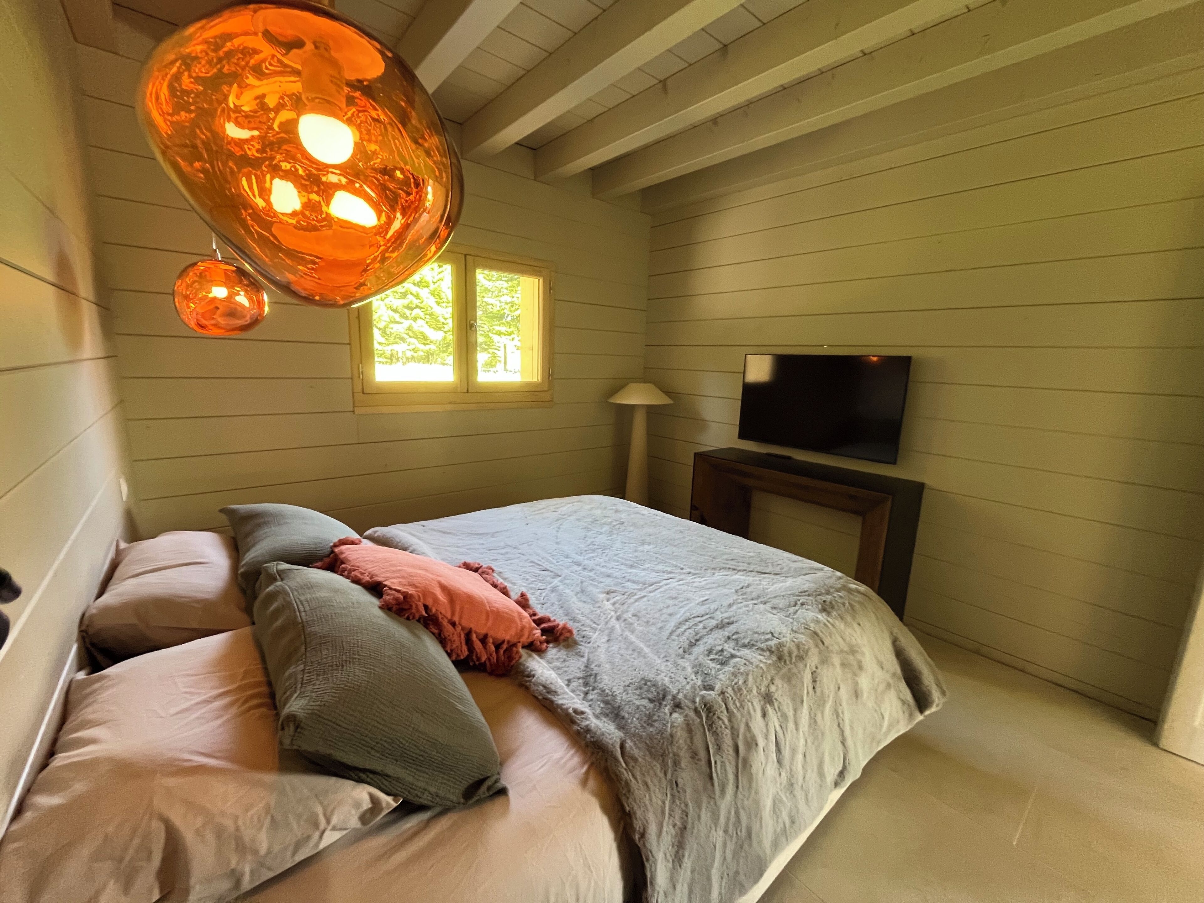 Un dormitorio con cama, almohadas, televisión y ventana.
