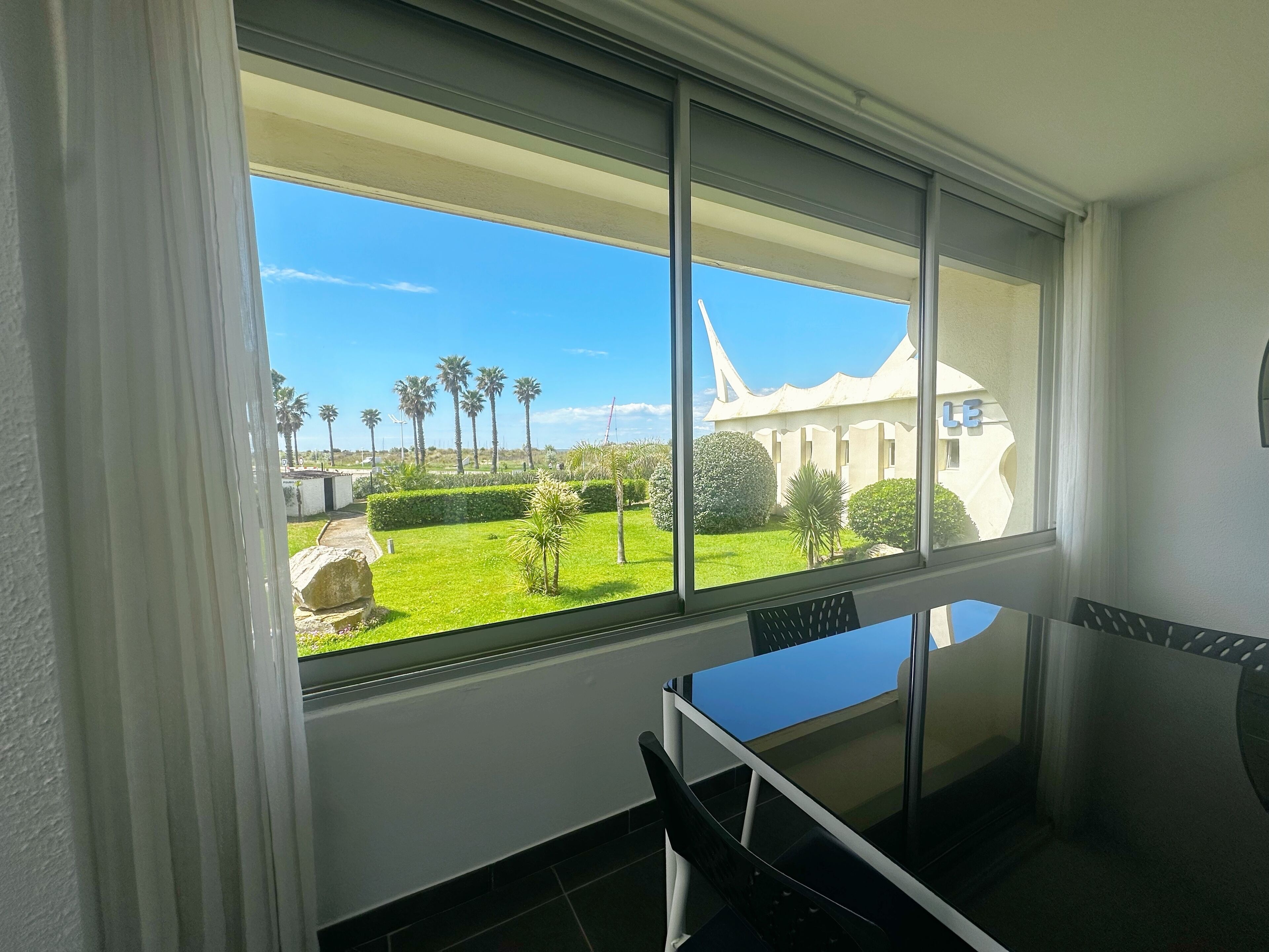 A room with a large window offering a view of a well-maintained garden and a white building with a unique architectural design.