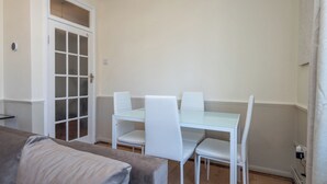 A small, well-lit room with a glass-top dining table, white chairs, and a beige sofa.