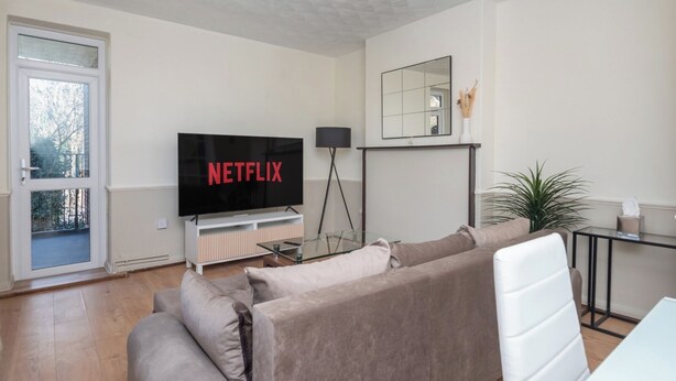 A modern living room with a flat-screen TV, a glass coffee table, a sofa, and a dining area with a small table and chairs.