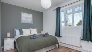 A bedroom with a bed, a nightstand, a bedside table, a radiator, and a window with curtains.