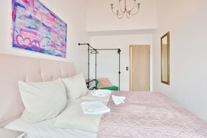 A bedroom with a bed, pillows, a hanging chair, a painting, a mirror, and a chandelier.