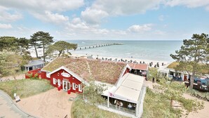 A coastal hotel with a red building, beach view, and a pier in the background. - Residence Ostseestrand Apartment 31 "Aurora" - Residence Ostseestrand (Scharbeutz)