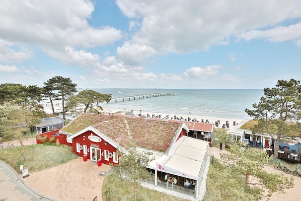 A coastal hotel with a red building, beach view, and a pier in the background.