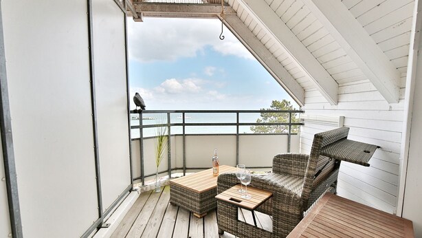 A balcony with wicker furniture, a table, and a bottle. - Residence Ostseestrand Apartment 31 "Aurora" - Residence Ostseestrand (Scharbeutz)