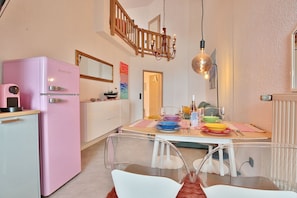 A compact kitchen with a pink refrigerator, a dining table set with colorful plates, and a chandelier.