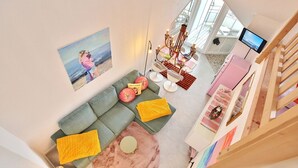 A modern living room with a green sofa, yellow cushions, a pink rug, and a painting of a woman on the wall. - Residence Ostseestrand Apartment 31 "Aurora" - Residence Ostseestrand (Scharbeutz)