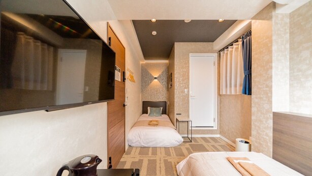 Une chambre d’hôtel de taille réduite, comprenant un lit, un petit bureau, une bouilloire et un miroir.