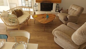 A cozy living room with a wicker sofa, a wooden coffee table, and a beige armchair. A flat-screen TV is mounted on the wall above a fireplace. - Secluded vineyard with jacuzzi (Beaulieu-sur-Loire)