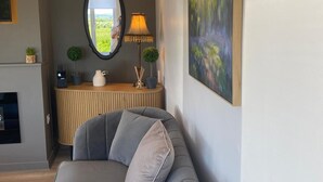Un salon moderne avec un canapé gris, un miroir rond, une lampe et un tableau accroché au mur.