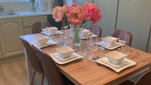 Une table à manger dressée avec des bols, des assiettes et des verres blancs, agrémentée d’un vase rempli de fleurs roses.