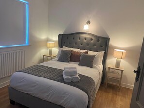 A neatly made bed with a grey quilt, white linens, and a rolled towel on top. There are two bedside lamps on wooden nightstands. - Luxurious 4-bed House in Tipperary Town (Tipperary)