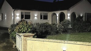 Une maison à deux étages, dotée d’une façade symétrique, de fenêtres en arc de cercle et d’une pelouse bien entretenue.