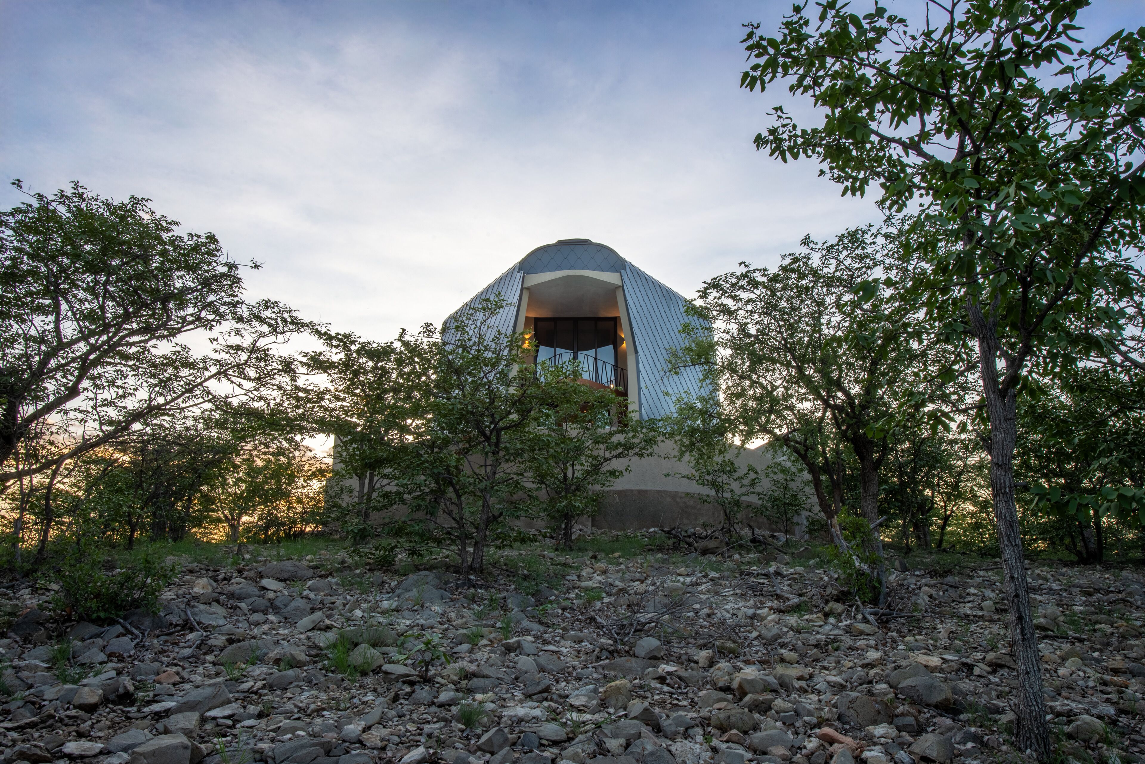 A dome-shaped building with a central entrance, surrounded by trees and rocky terrain.