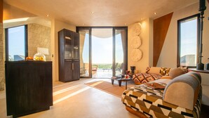 A modern living room with a sofa, a coffee table, and a kitchen area with a dark cabinet. - The Ekipa (Okaukuejo)