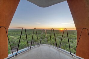 A room with a concrete floor, metal railings, and a view of a green landscape at sunset. - The Ekipa (Okaukuejo)