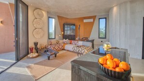 A modern living room with a sofa, coffee table, and a bowl of oranges on a counter. - The Ekipa (Okaukuejo)
