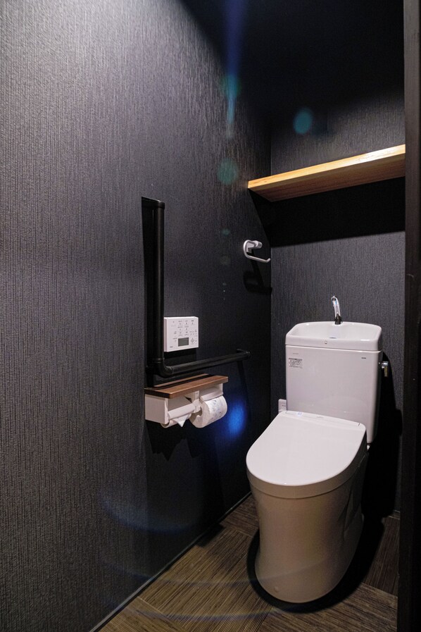 Une salle de bain moderne et compacte, équipée de toilettes, d’un lavabo fixé au mur et d’un panneau de commande.