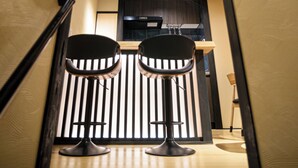 Un couloir étroit, avec deux tabourets de bar noirs et un comptoir en bois au fond.