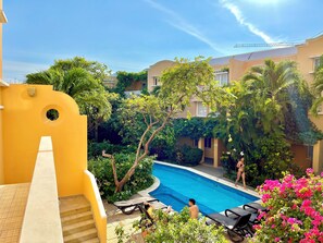 A pool area with lounge chairs and a staircase leading to a building with a yellow facade. - by Calamari Homes - Edificio Centenario (Cartagena)