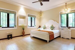 Un dormitorio con una cama grande, mesitas de noche, ventilador de techo y ventanas con persianas.