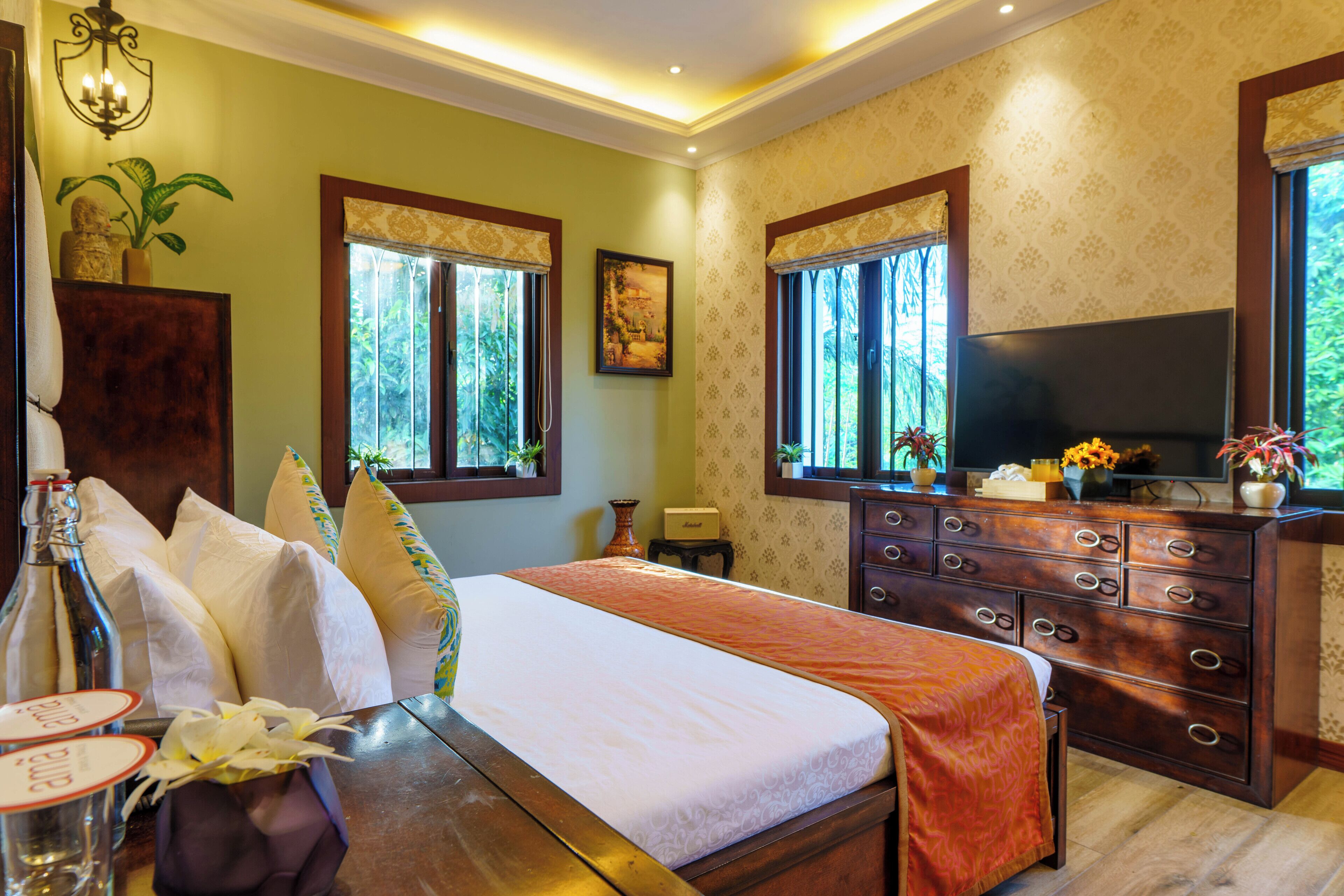 A hotel room with a large bed, a wooden dresser, a television, and large windows.