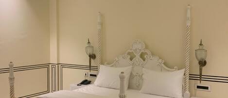 A four-poster bed with a white headboard, a bedside table with a lamp, and a yellow armchair.