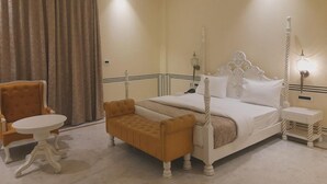Una camera d'albergo con un letto a baldacchino, un tavolino rotondo, una panca e un comodino.