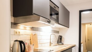 A compact kitchen with a washing machine, a coffee maker, and a kettle on the counter.