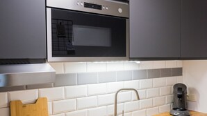 A modern kitchen with grey cabinets, a stainless steel microwave, a wooden cutting board, a sink, and a coffee maker.