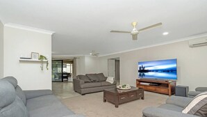 A modern living room with grey sofas, a coffee table, a flat-screen TV, and a ceiling fan.