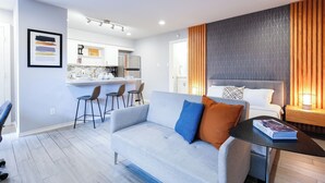 A modern living room with a grey sofa, a coffee table, and a dining area with a kitchen in the background.