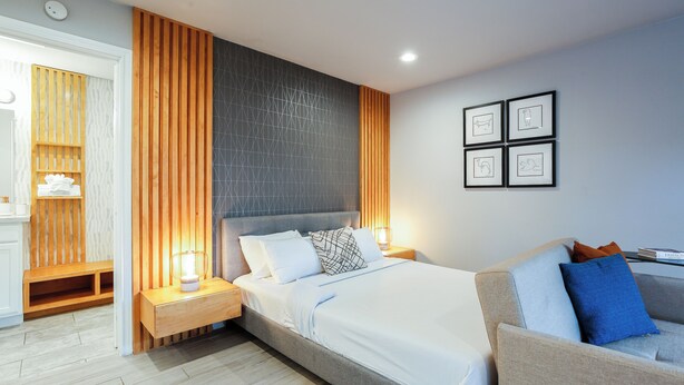 A modern bedroom with a bed, a sofa, a nightstand, and a wall with framed pictures.