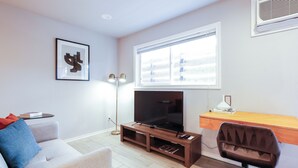 A living room with a sofa, a TV on a wooden stand, a desk, and a chair.