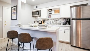 A modern kitchen with white cabinets, a stainless steel refrigerator, and a bar area with stools.